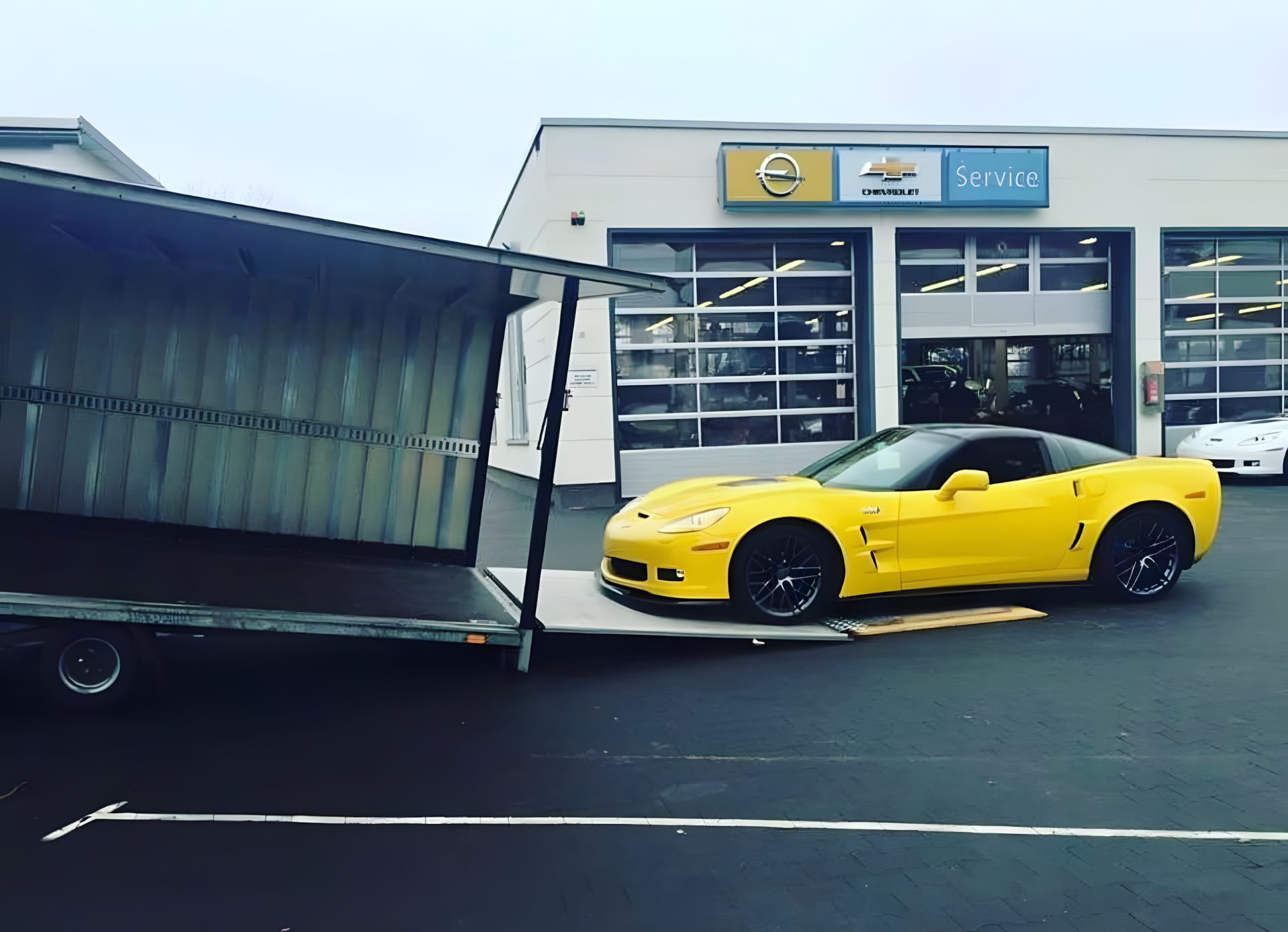 Anlieferung einer Corvette per geschlossenem Transporter vor einem Autohaus – Fahrzeugtransport für Händler